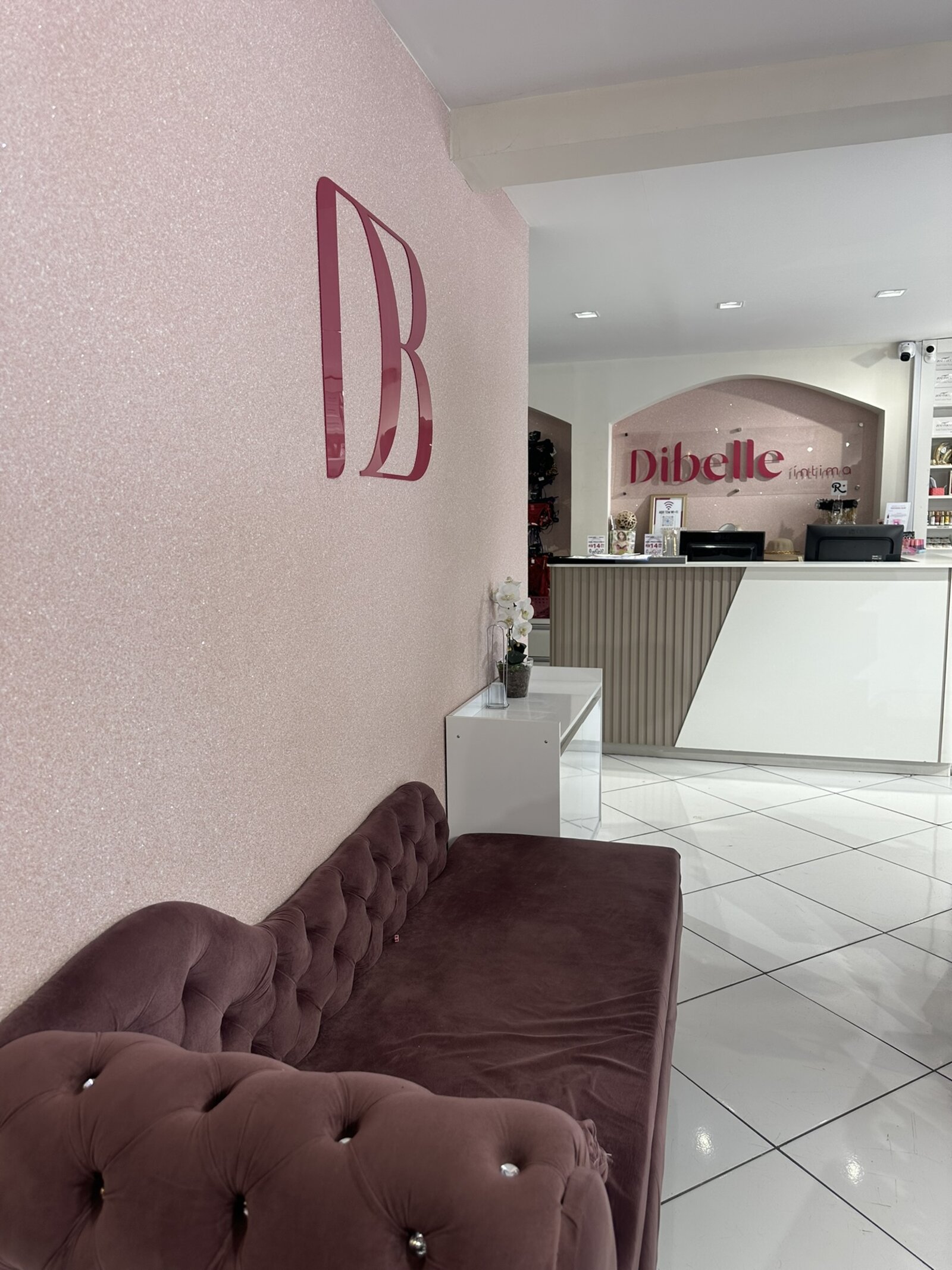 Interior da loja Dibelle Íntima: parede rosa com o monograma DB e o balcão de atendimento