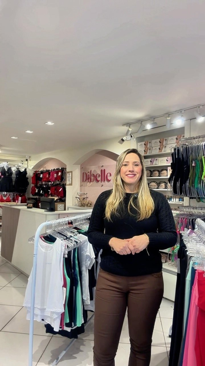 Interior da loja Dibelle Íntima, com araras de peças e a parede rosa com a marca
